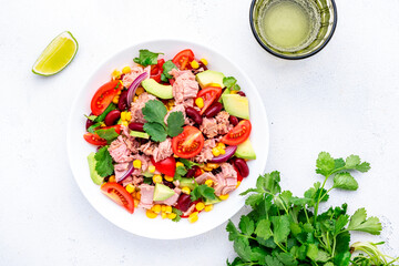 Mexican style salad with canned tuna, avocado, corn, red beans, cherry tomatoes and cilantro, white table background, top view