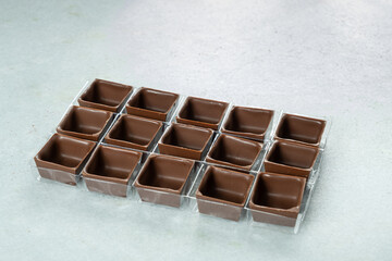 Square-shaped milk chocolate shells inside the molds.