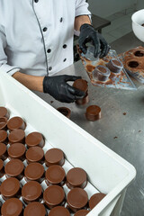 Circular chocolate shells ready to be filled with a worker in the background unmolding the shells_vertical.