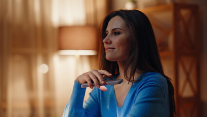 Smiling brunette texting mobile phone in dark apartment closeup. Relaxed woman