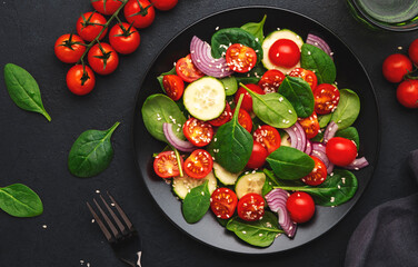 Healthy salad with spinach, tomatoes, cucumber, onion, sesame and olive oil, top view