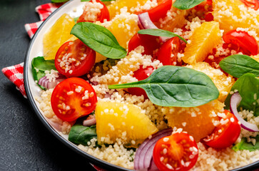 Gourmet vegan salad with couscous, tomatoes, onion, spinach and orange. Black background, top view