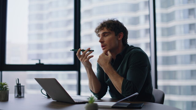 Businessman recording audio message talking to cellphone loudspeaker at office.