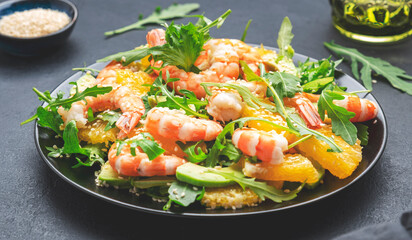 Seafood salad with shrimps, avocado, juicy orange, fresh arugula and sesame on black table, top view