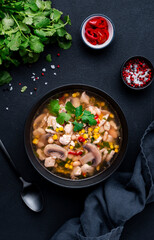Mexican style chicken soup with mushrooms, corn, white beans, hot chili and cilantro. Black table background, top view