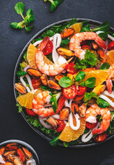 Delicious seafood salad with shrimp, mussels, squid, oranges, lettuce and olive oil with lemon dressing, black background, top view