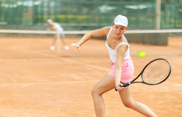 Young woman playing tennis against female opponent on tennis court