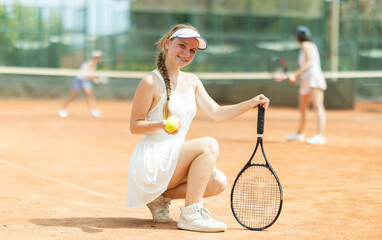 Woman in sportswear against backdrop of outdoor tennis court. Team players pose on sports ground