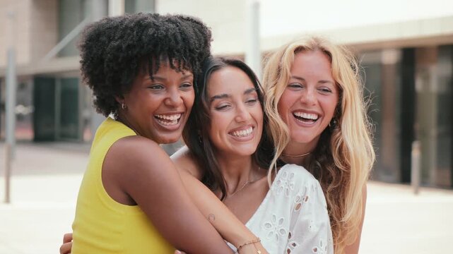 Three multiracial young women laughing, smiling and embracing together on a friendly meeting. Group of diverse girls having fun giving a hug on a social gathering with happiness and love expression