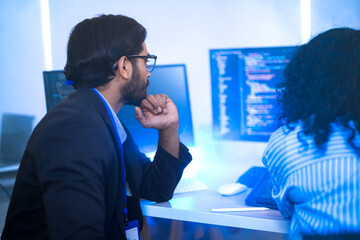 Diverse AI tech team reviewing code for a machine learning algorithm. Indian male and Hispanic female programmers collaborating on artificial intelligence development.