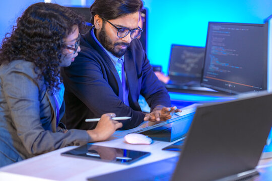 Diverse team of AI developers collaborating in a modern office. Indian male leading a discussion with Asian and Hispanic female colleagues on a machine learning project.