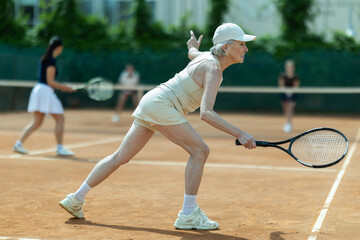 Elderly female tennis player playing doubles tennis on tennis court
