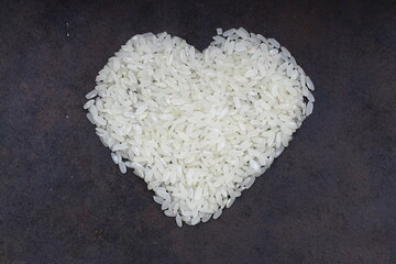 Heart-shaped rice on dark background. Love and valentines day concept. Raw long white rice in shape of heart. Traditional Asian food.