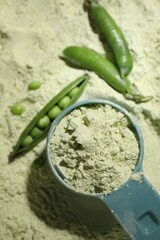 Measuring spoon and fresh pea pods on protein powder, flat lay