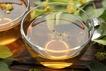 Fresh linden tea in cups and flowers on wooden table, closeup