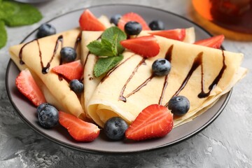 Tasty crepes with berries, chocolate sauce and mint on gray textured table, closeup