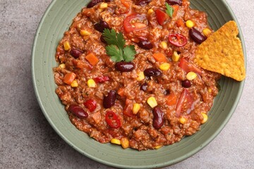Tasty chili con carne in bowl and nachos on grey table, top view