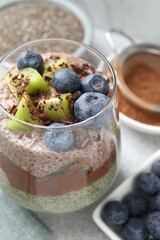 Delicious chocolate pudding with chia seeds, kiwi and blueberries in glass on grey table, closeup