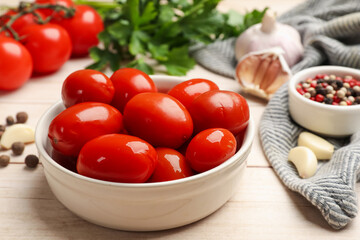 Tasty pickled tomatoes in bowl and ingredients on light wooden table, closeup