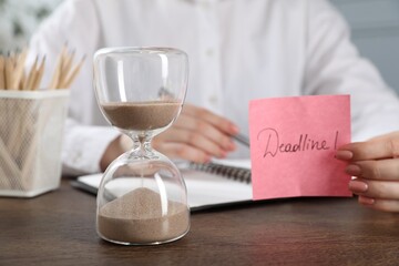 Woman holding sticky note with word Deadline at wooden table in office, closeup