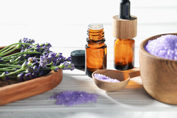 Bottles of lavender essential oil, sea salt and flowers on white wooden table, closeup