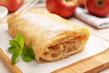 Tasty apple strudel with powdered sugar, mint and fruits on table, closeup