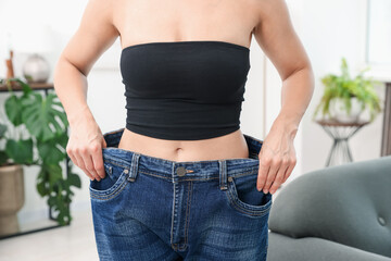 Fit woman wearing old jeans after weight loss at home, closeup