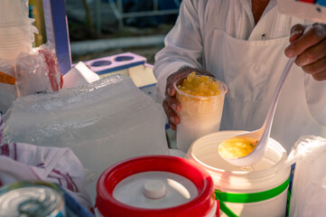 Artisanal shaved ice vendor prepares a portion, adding pineapple and other artisanal tropical...