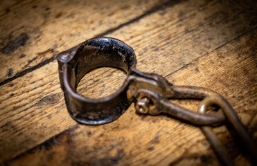 Ancient iron handcuff and chain on wooden floor from medieval times in England, prisoner wrist restraint.