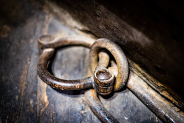 Ancient medieval iron prisoner restraint, possibly fetter or leg cuff, on wooden floor.