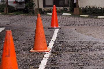 ground-level view of three orange traffic cones arranged on an asphalt surface. A white line is...