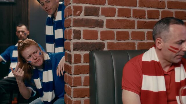 Young football fans in red sports uniform expressing despair about failure of their favorite team after watching match broadcast while people in blue t-shirts mocking them and laughing