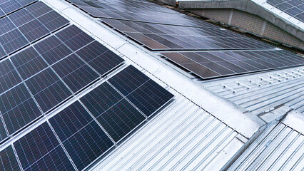 Obraz premium Aerial view of photovoltaic solar panels installed on the metal roof of a commercial building or factory. Concept of renewable energy, sustainable technology, and green power generation.