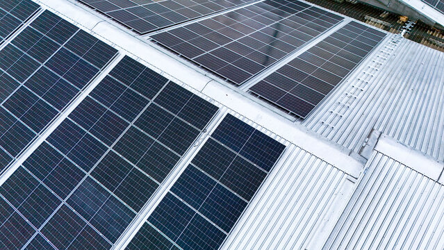 Aerial view of photovoltaic solar panels installed on the metal roof of a commercial building or factory. Concept of renewable energy, sustainable technology, and green power generation.