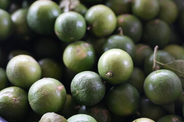 many fresh green limes piled together. The limes have vibrant green color with slightly rough natural skin texture, showcasing freshness and quality of agricultural produce. Perfect for cooking