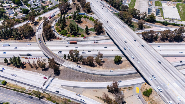 Top-down drone view of highway interchange in Los Angeles, California, showing looping on-ramps, heavy vehicle traffic, and layered roads in a modern urban infrastructure setting