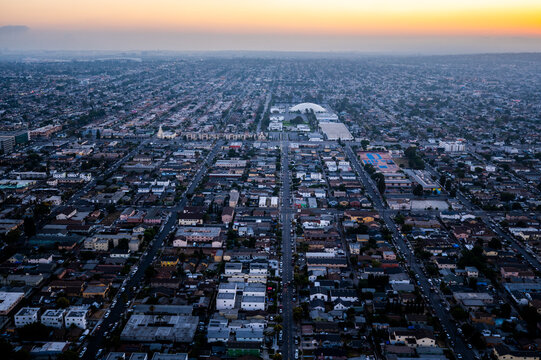 Expansive aerial view of Los Angeles at sunset with rows of homes, urban grid layout, and distant haze on the horizon in warm evening light