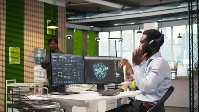 Software developer testing generative AI machine learning algorithms and listening music at work. African american man wearing headphones scaling productivity with AI large language model, camera A