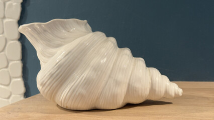 White ceramic conch shell decoration on a wooden shelf