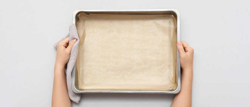 Woman holding baking tray with paper on grey background, closeup