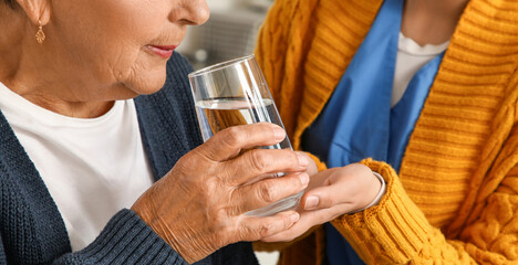 Senior woman taking glass of water from caregiver, closeup