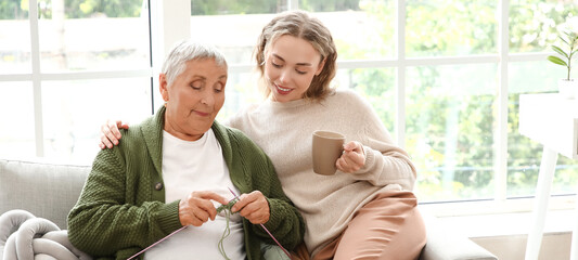 Senior woman knitting with her granddaughter on sofa at home
