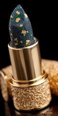 Close up of a luxuriously decorated lipstick with gold flecks and blue green accents on a black background