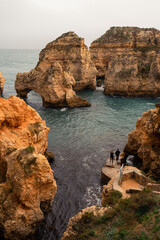 Tourists walk along the water's edge on a beautiful sandy beach, nestled between the towering...