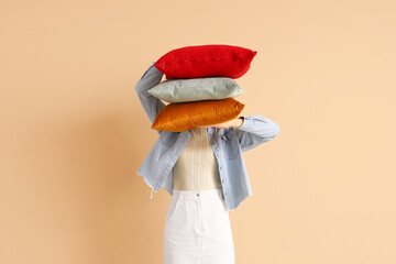 Woman with stack of pillows on beige background