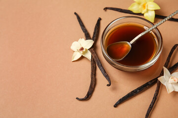 Vanilla extract in bowl with spoon, vanilla pods and flowers on beige background