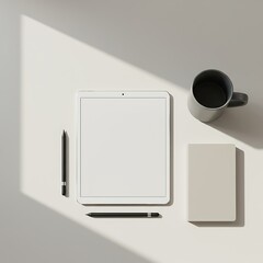 Overhead view of a tablet, pens, notebook, and coffee mug on a white surface.
