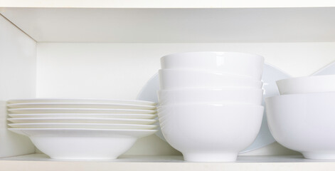 White dishes and bowls in a kitchen cabinet.