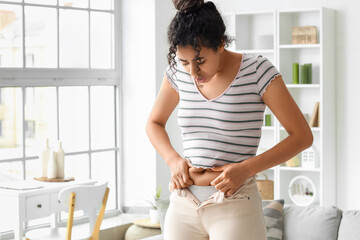Young African-American woman in tight pants at home. Diet concept