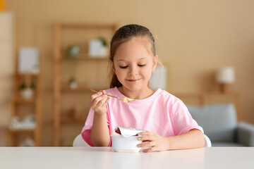Cute little girl sitting by table and eating yogurt at home